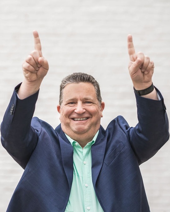 Brian Watkins, founder of BTOM Consultants, smiling and pointing up with both hands